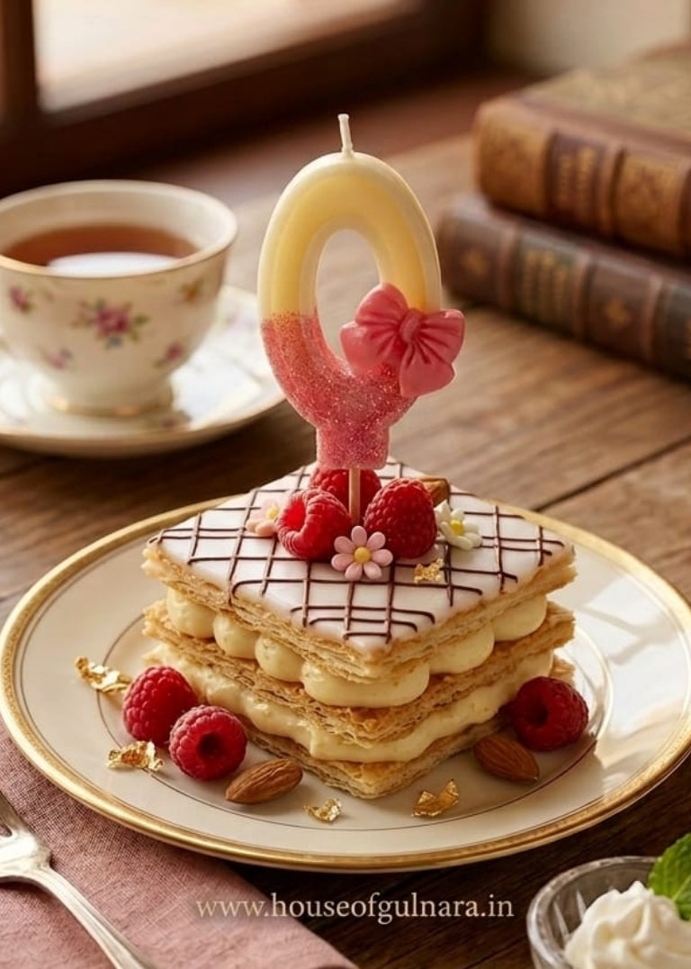 Stack of pancakes with a candle on a plate, accompanied by a cup of tea and a fork on a wooden table.