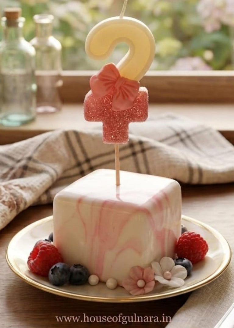 Small cake with a number two candle on a plate, set against a window with flowers in the background.