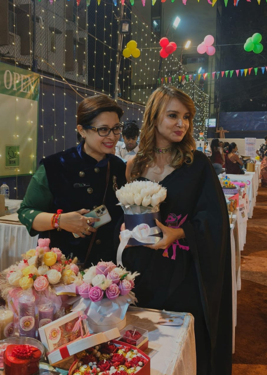 Two women standing next to a table with candle bouquets and gifts at an event with colorful decorations.
