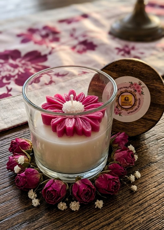 Candle with a pink flower-shaped candle wick on a wooden surface with dried flowers.