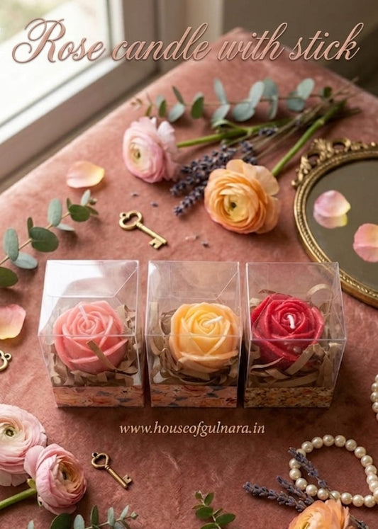 Three rose-shaped candles in clear packaging on a decorative surface with flowers and keys.
