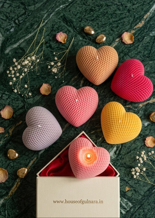 Colorful heart-shaped candles on a dark surface with flowers and a box.