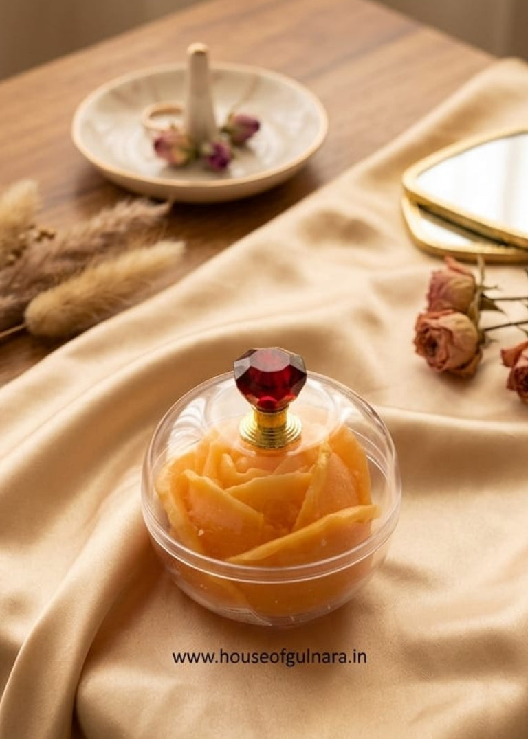 Decorative rose-shaped container with a red gem on a beige fabric surface.