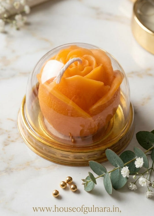 Decorative orange rose in a glass dome on a marble surface with eucalyptus leaves and a gold strainer.